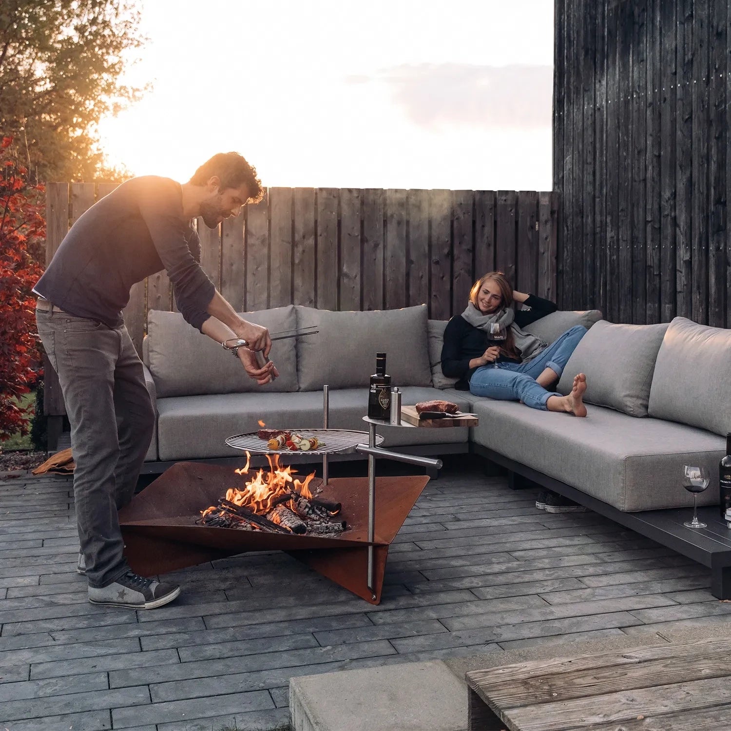 Höfats TRIPLE 120 Fire Pit in Corten Steel with burning logs, placed on a white surface.