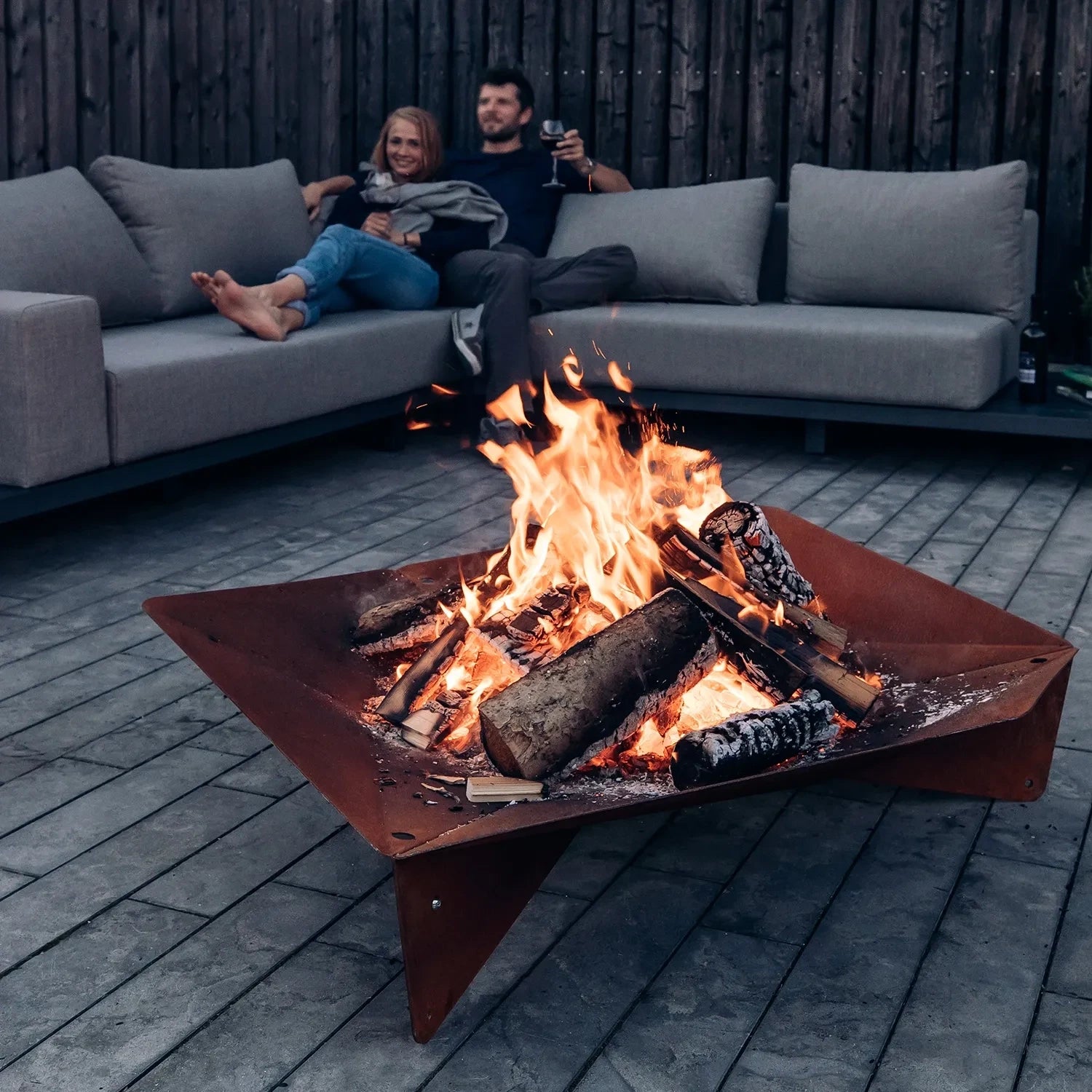 Höfats TRIPLE 120 Fire Pit in Corten Steel with burning logs, placed on a white surface.